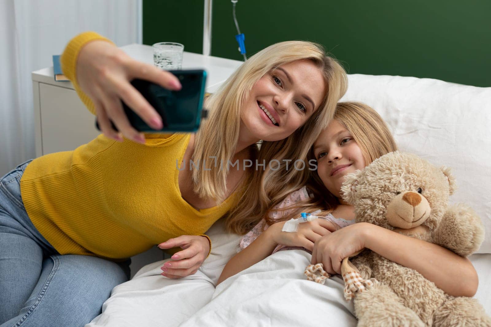 A loving mother and her daughter joyfully share a cheerful moment as they take a delightful selfie in a hospital room