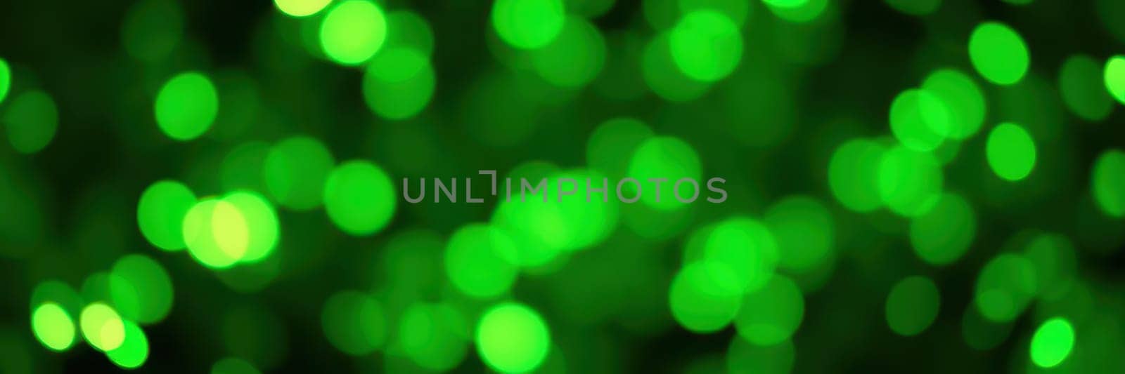 Colorful bokeh lights twinkle in various shades of green, illuminating a lively outdoor gathering in a city park during the evening. The ambiance feels joyful and celebratory.