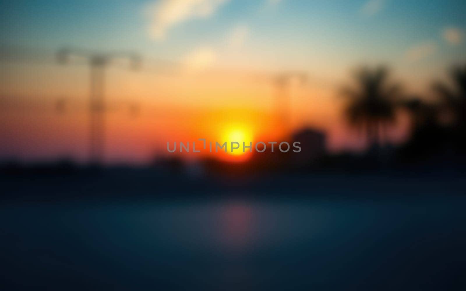 As the sun sets on the horizon, vibrant colors blend in the sky, casting a warm glow over a tropical landscape featuring silhouetted palm trees and power lines.