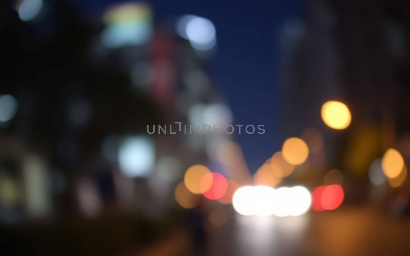 Bright city lights create a beautiful bokeh effect as vehicles move along the street at night, highlighting the dynamic atmosphere of urban life after sunset.