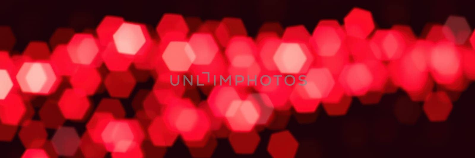 Red hexagonal lights shimmer in a blurred pattern, creating a vibrant and festive atmosphere during a celebratory evening event. The glow enhances the joy of the gathering.