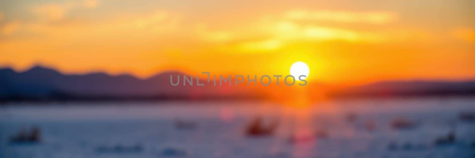 A colorful sunset illuminates the sky and reflects on the water's surface, with silhouettes of boats scattered across the serene landscape, accompanied by distant mountains.