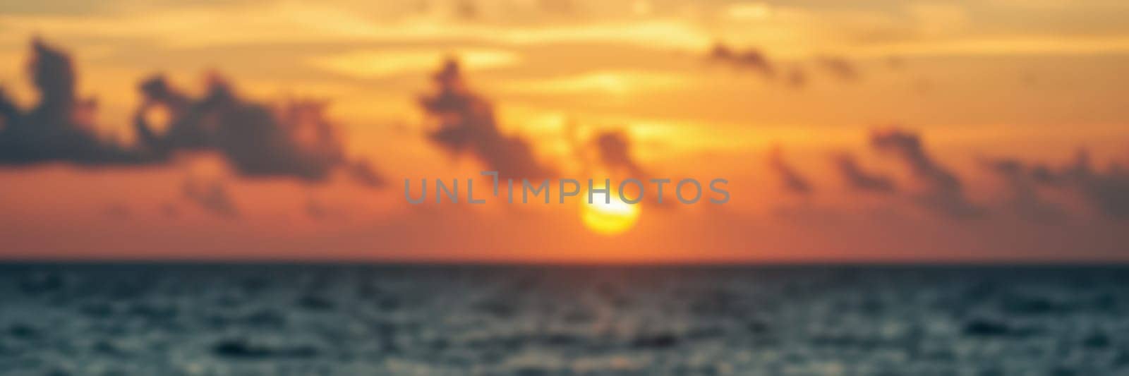 A breathtaking sunset unfolds over the ocean, featuring brilliant hues of orange and yellow blending into the sky. Gentle waves reflect the fading light during the evening.