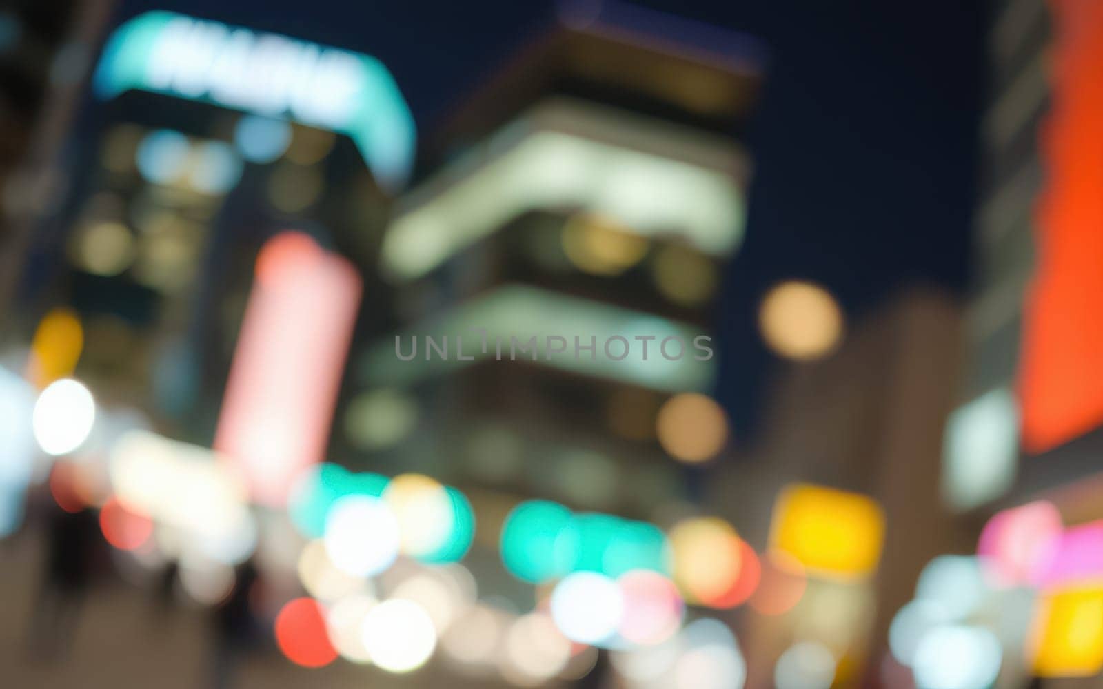 A lively urban area filled with colorful lights and blurred movement as people walk through the streets during a vibrant evening. The atmosphere is electric as the city comes alive.