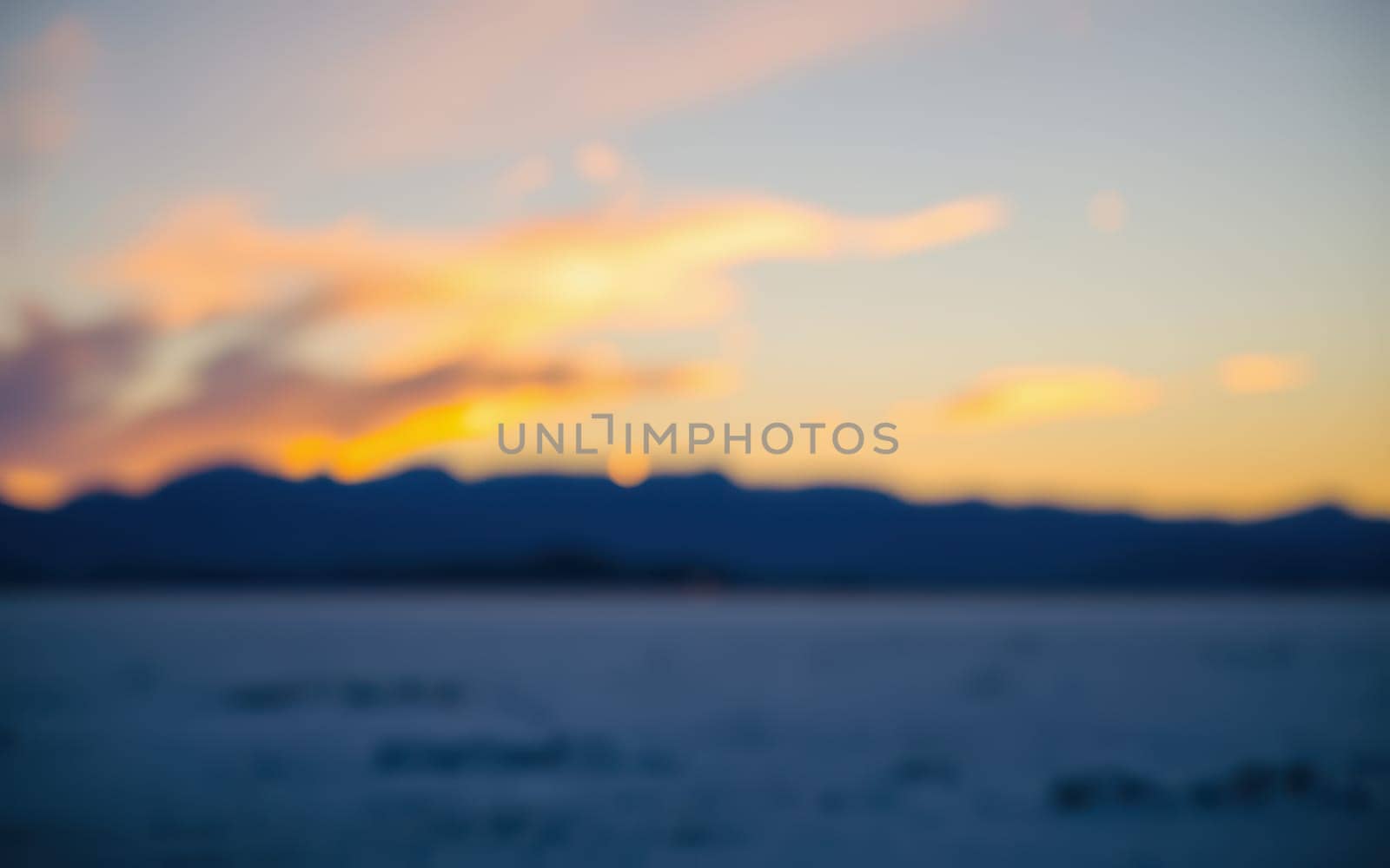 A stunning sunset paints the sky with vibrant hues while the silhouette of mountains frames the ocean below. The soft focus adds a serene quality to the scene captured just before nightfall.