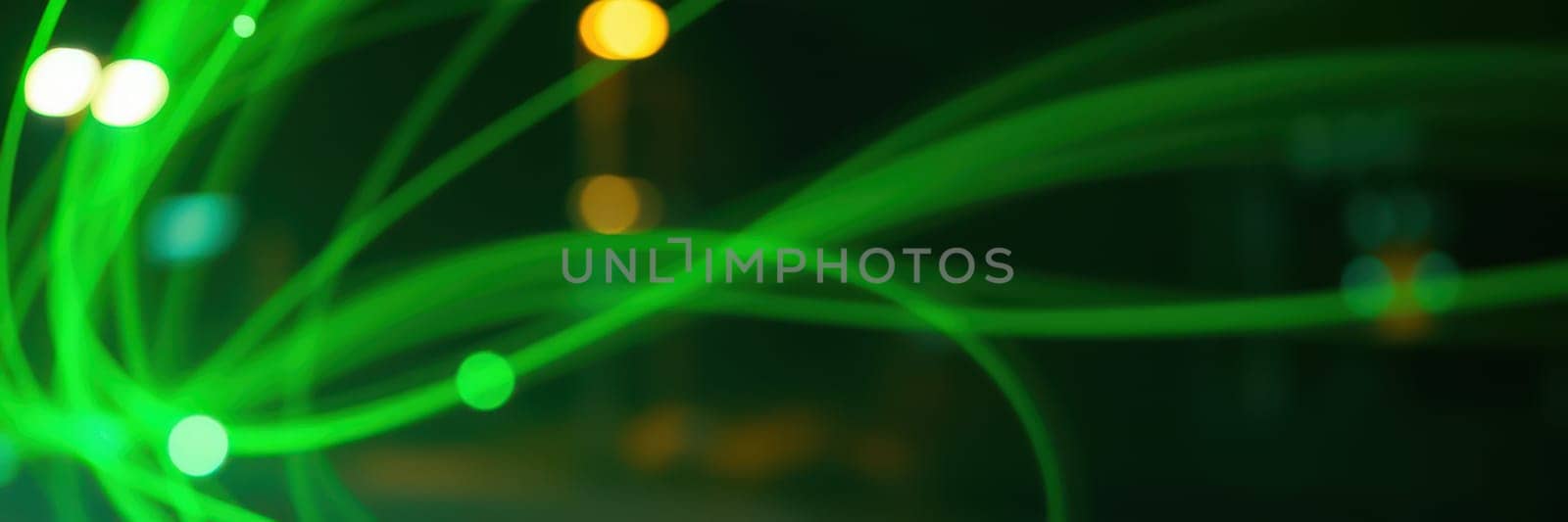 Colorful green light trails create dynamic patterns against a dark backdrop during an evening event. The ambiance is lively, enhancing the atmosphere with energy.
