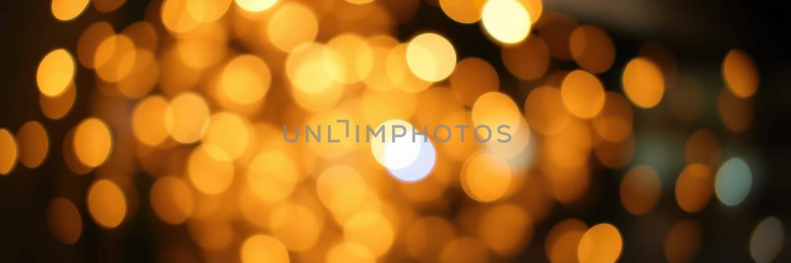 Shimmering golden lights illuminate an outdoor space, enhancing a joyful ambiance during evening festivities. People mingle and celebrate together under the glowing lights.