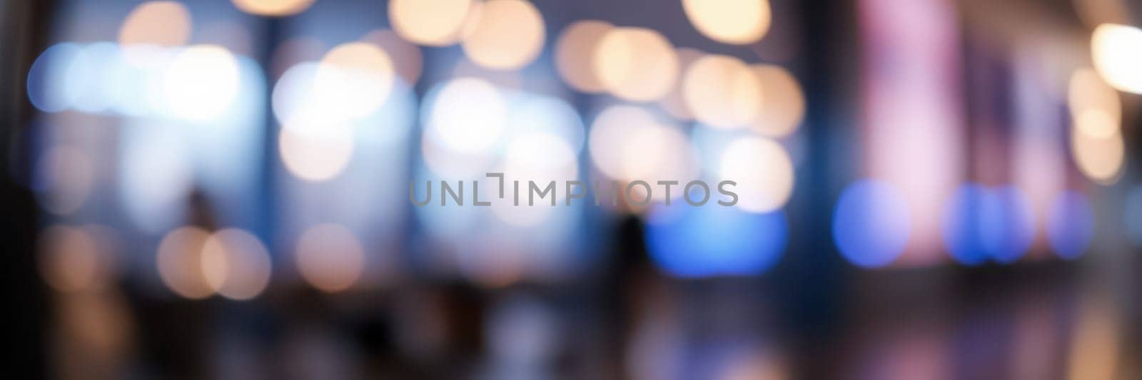 Warm lights create a cozy atmosphere in a busy urban area as silhouettes of people move through the space, enjoying the evening ambiance.