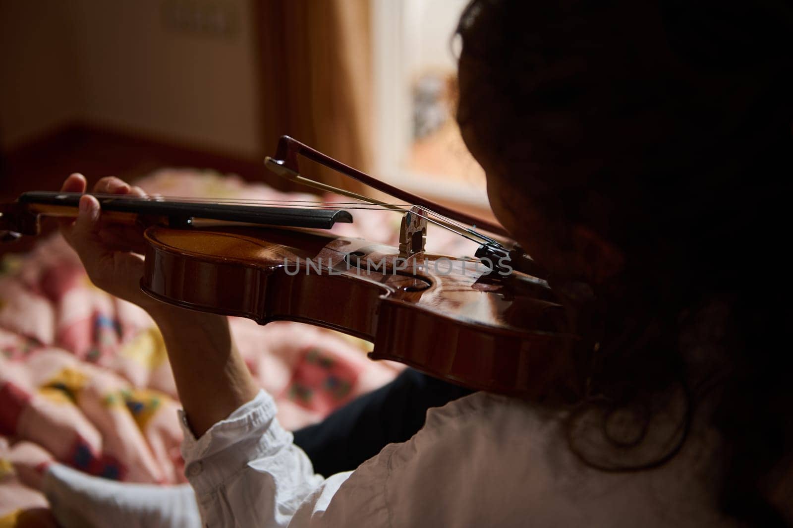 A detailed view of a person playing the violin indoors, surrounded by warm, intimate lighting.