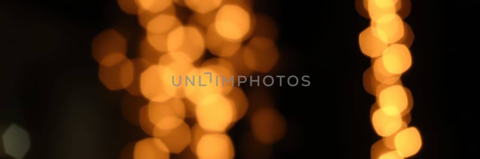 Colorful bokeh lights twinkle in a dark urban environment, adding a warm and inviting glow to the night. The vibrant orbs create a cheerful ambiance for local festivities.
