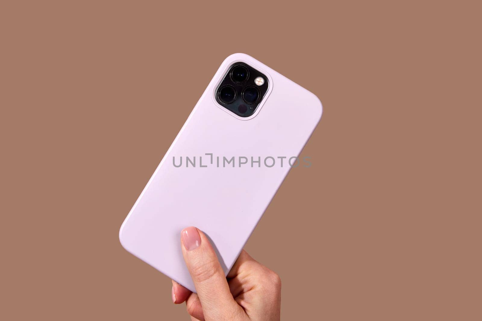 Hand holding sleek purple smartphone featuring multiple camera lenses against a rich brown background, highlighting modern mobile technology design elements Mocha Mousse color of 2025 year