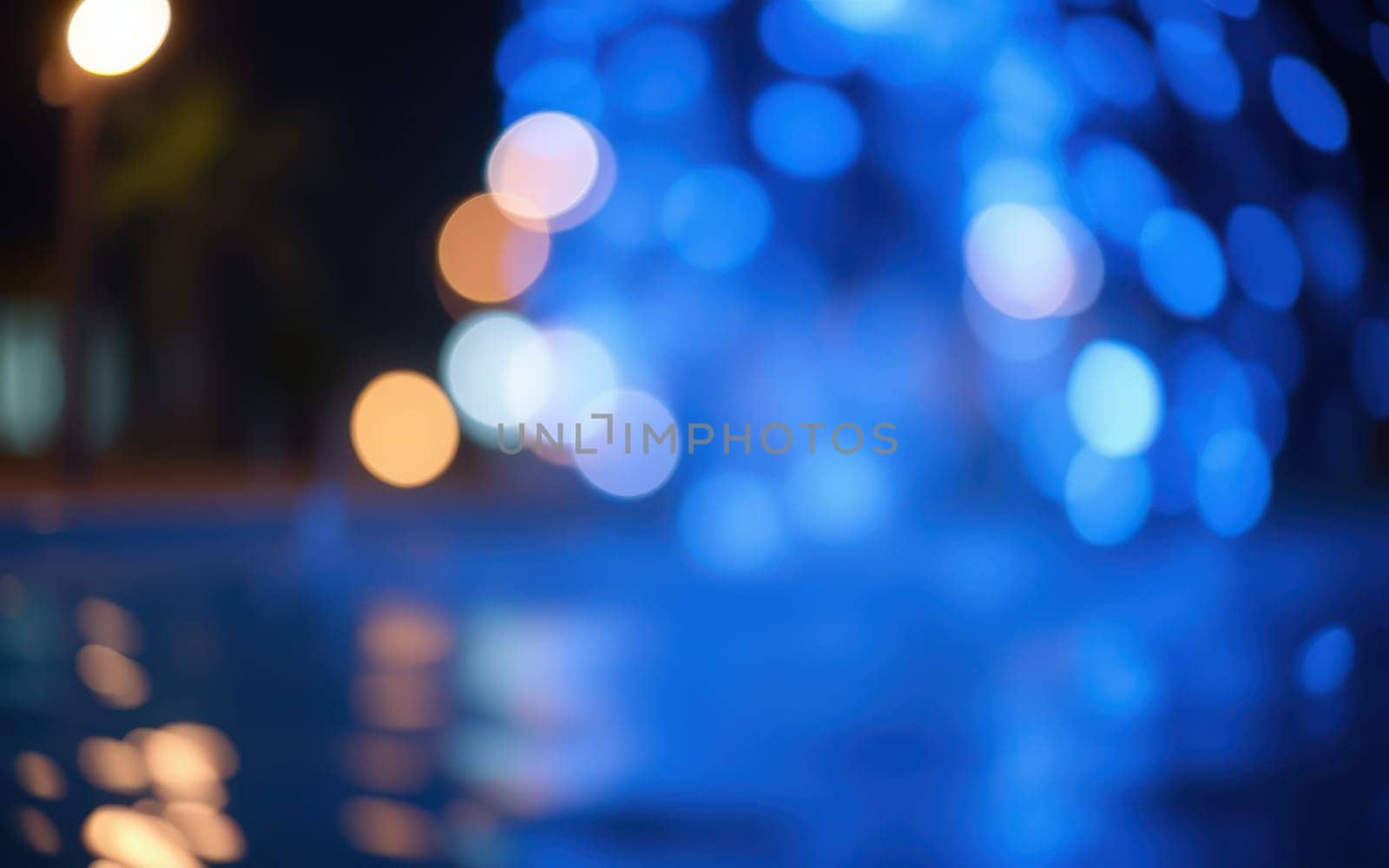 A fountain with bright blue lights sprays water, creating a lively ambiance near a pool at night. The surrounding lights reflect on the water, enhancing the scene.
