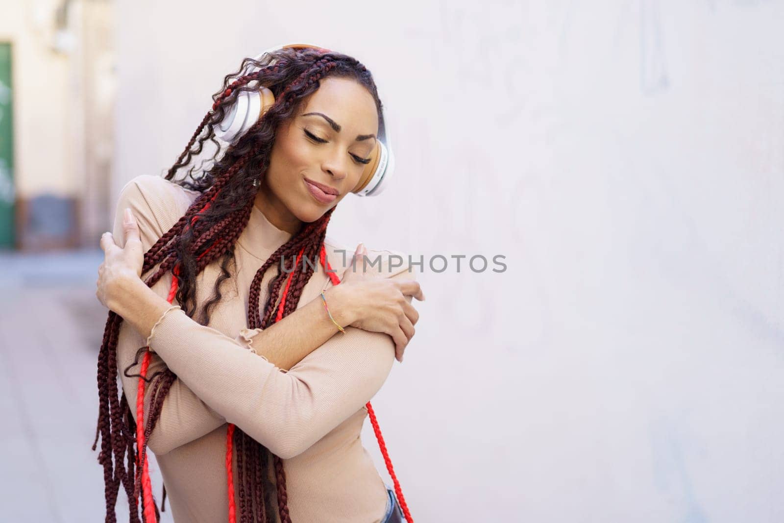 In a lively urban environment, a joyful woman with long, beautiful braids listens to her favorite tunes through her stylish headphones, joyfully radiating feelings of happiness and a sense of freedom