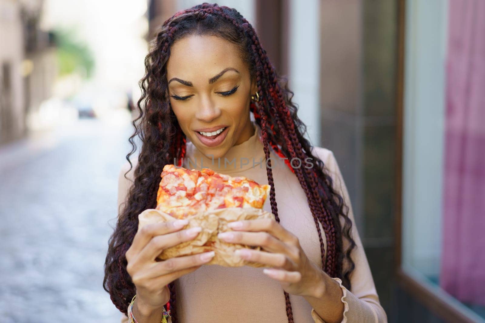 A joyful woman, full of energy and happiness, indulges in a delicious slice of pizza as she strolls down a charming city street, perfectly showcasing the delightful bliss of enjoying street food