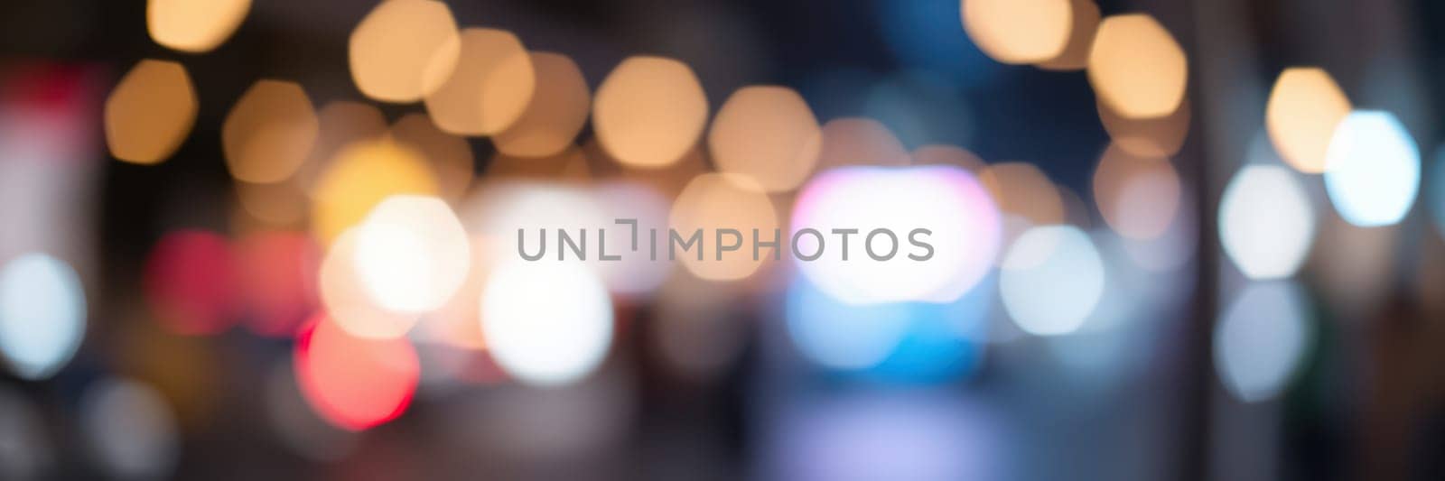 Colorful lights illuminate a busy street, creating a lively atmosphere. Various shapes and colors blend together, reflecting the energy of the city at night.