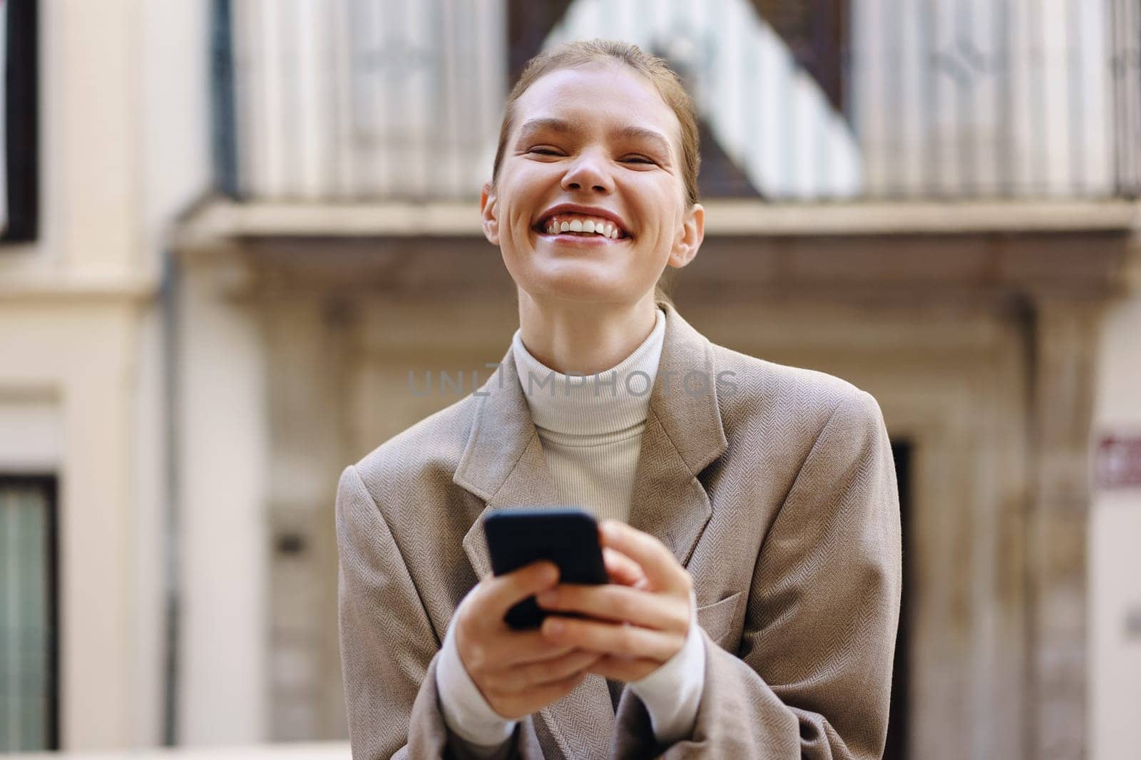 A joyful woman smiles brightly while checking her smartphone in an urban outdoor setting, radiating pure happiness and confidence, making the moment one of connection and delight in life