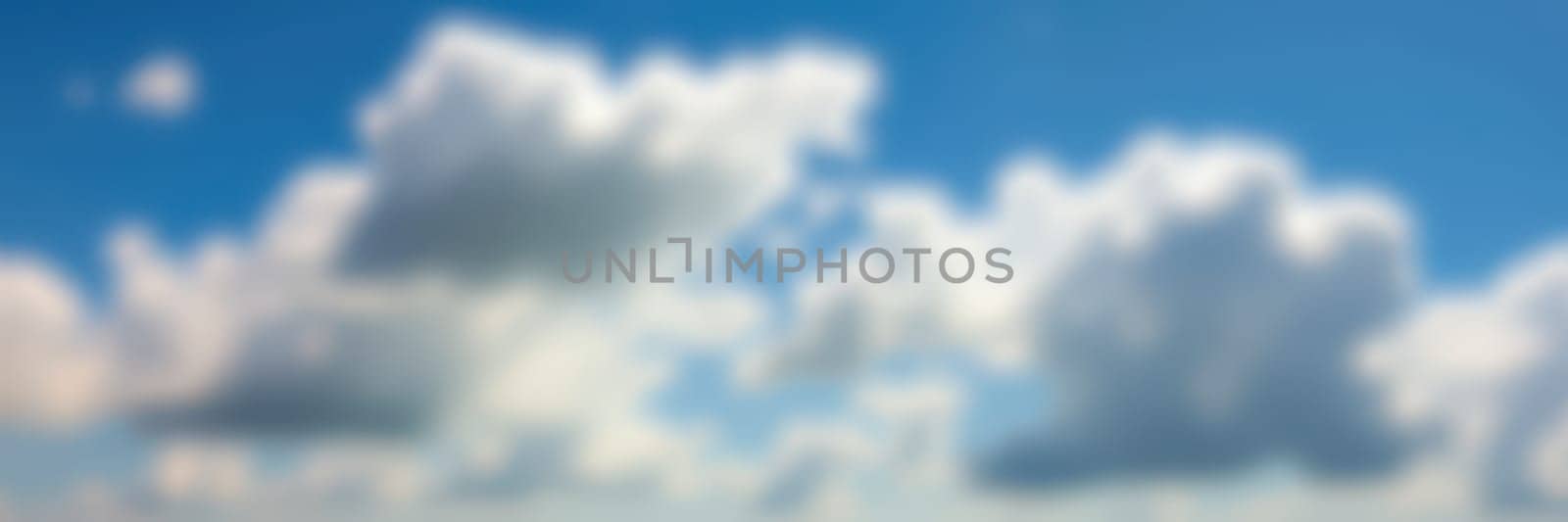 Fluffy white clouds float gently in a clear blue sky, casting shadows and providing a peaceful backdrop during a calm afternoon. The scene evokes a sense of serenity.