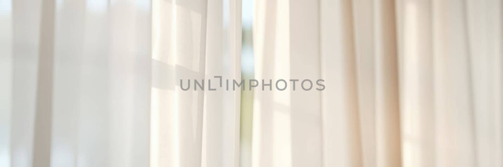 Sunlight softly pours into a bright room, creating a peaceful atmosphere as it passes through sheer white curtains, enhancing the lightness of the space.