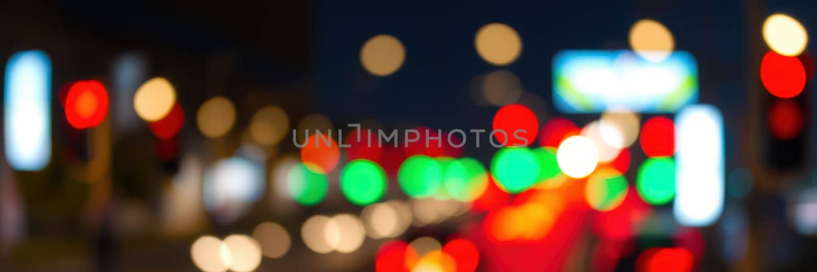 A bustling urban street at night features blurred traffic lights displaying vivid colors of red and green while vehicles move through the scene, adding energy.