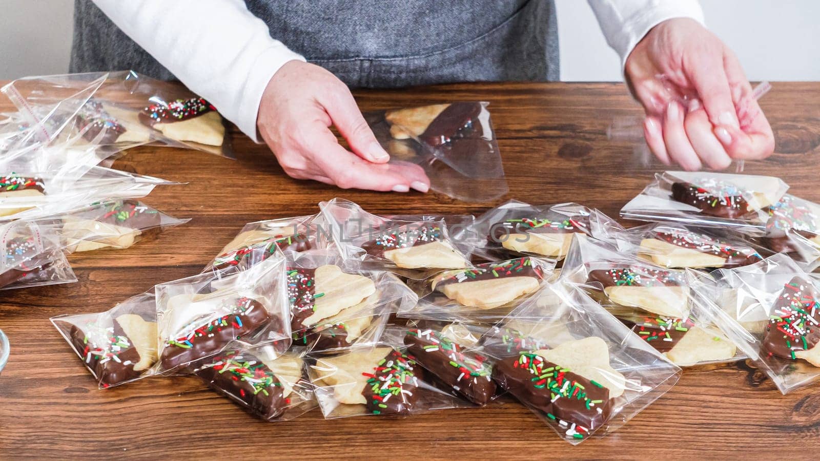 Carefully packaging Christmas cutout cookies, half-dipped in chocolate and presented in clear cellophane wrapping, perfect for festive gifting.