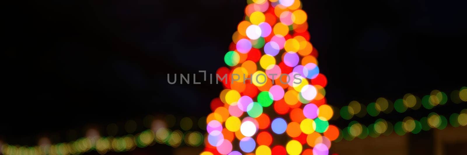 A dazzling Christmas tree glows with vibrant lights of various colors against a dark evening backdrop, creating a festive atmosphere for holiday gatherings.