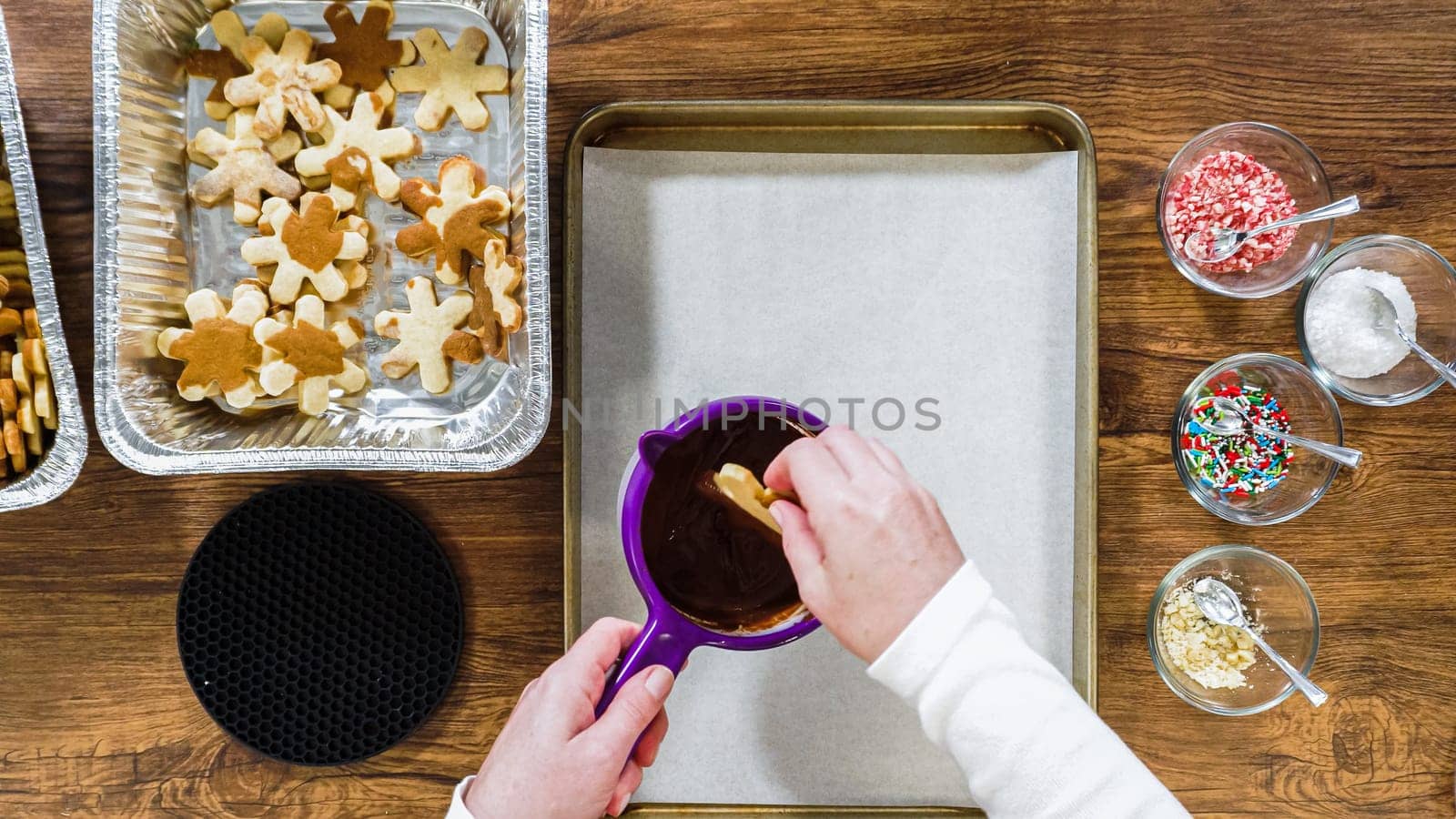 Flat lay. Creating snowflake-shaped cutout sugar cookies, dipped in chocolate, and adorned with different toppings.