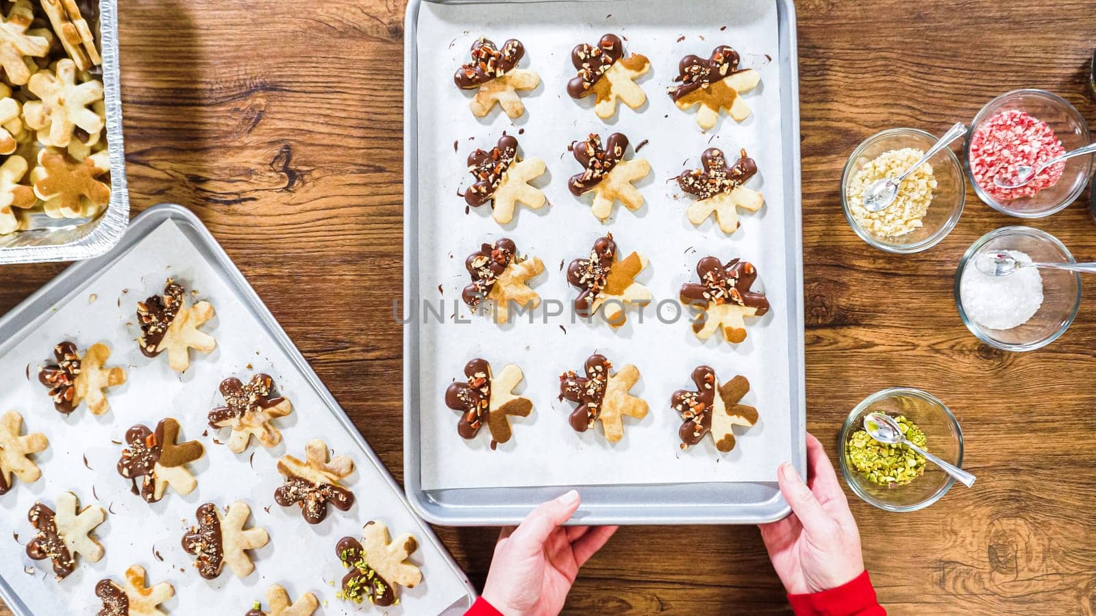 Flat lay. Carefully packaging Christmas cutout cookies, half-dipped in chocolate, sprinkled with crushed nuts, and presented in clear cellophane wrapping.