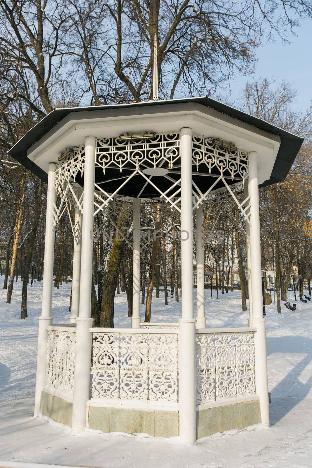 Beautiful white wooden gazebo in a winter park against the backdrop of snowy trees. Park within the city.