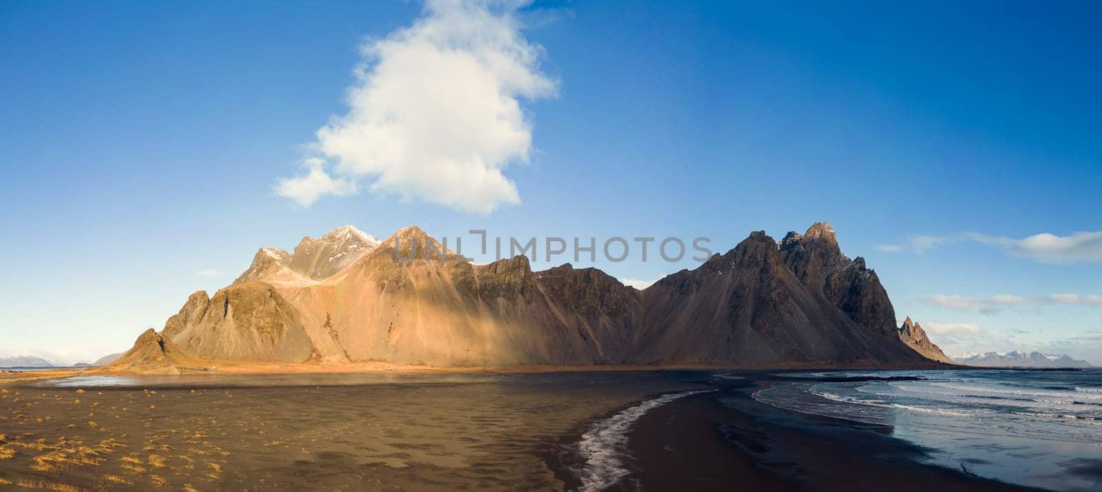 Panoramic view of vestrahorn rocky hills on icelandic peninsula, with unique black sand beach and nordic outdoor setting. Incredible landscape created by mountain top and ocean waves.