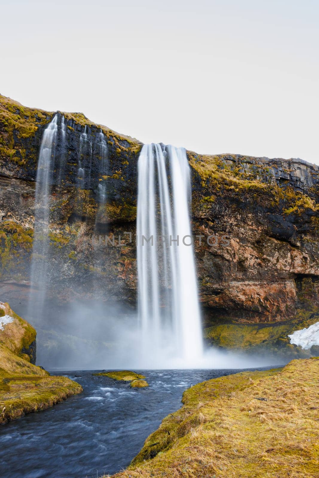 Picturesque icelandic cascade surrounded by high mountains and wonderful greenery. Seljalandsfoss waterfall rushes over an edge with freezing water and large stones, nordic destination.