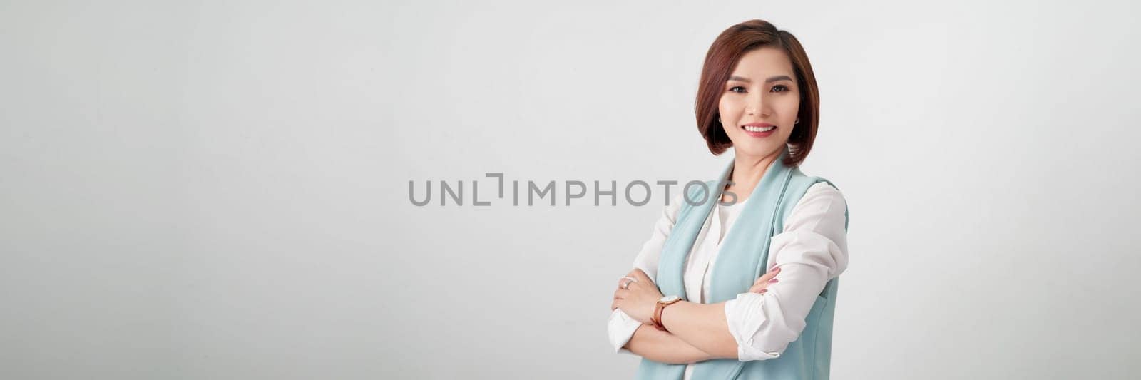 Smiling young beautiful Asian businesswoman doing arm crossed gesture in isolated white banner by makidotvn