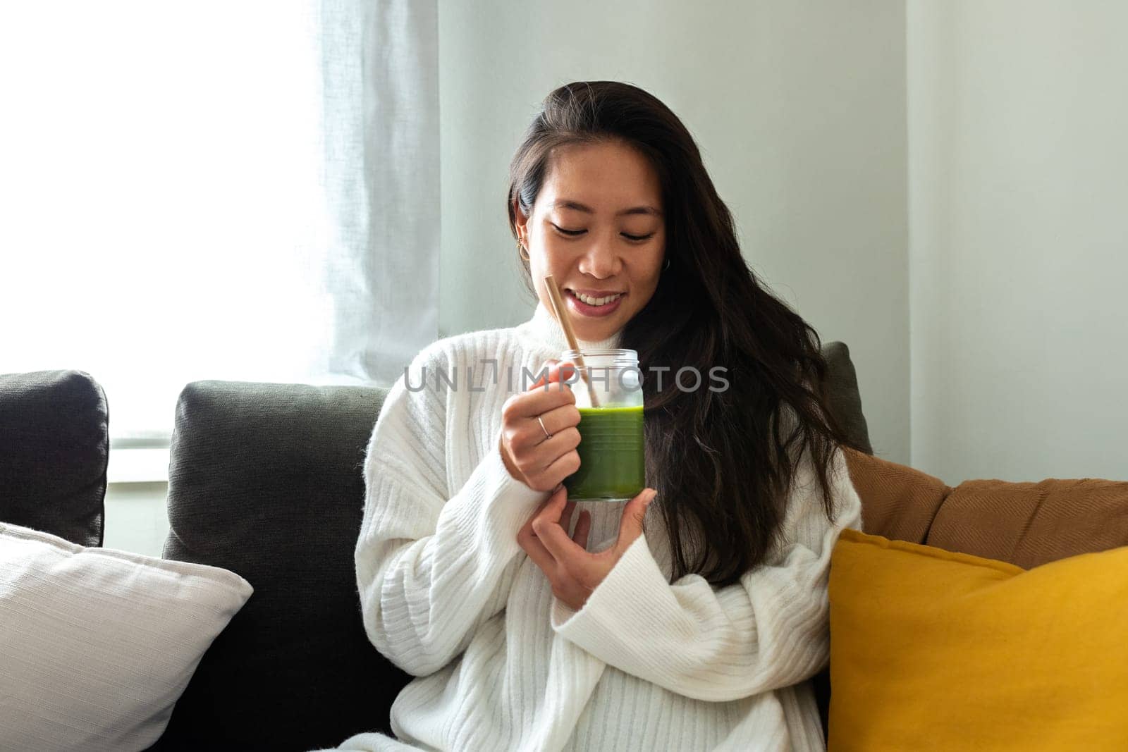 Beautiful young Asian woman relaxing at home drinking vegetable healthy green smoothie. Healthy eating and lifestyle concepts.