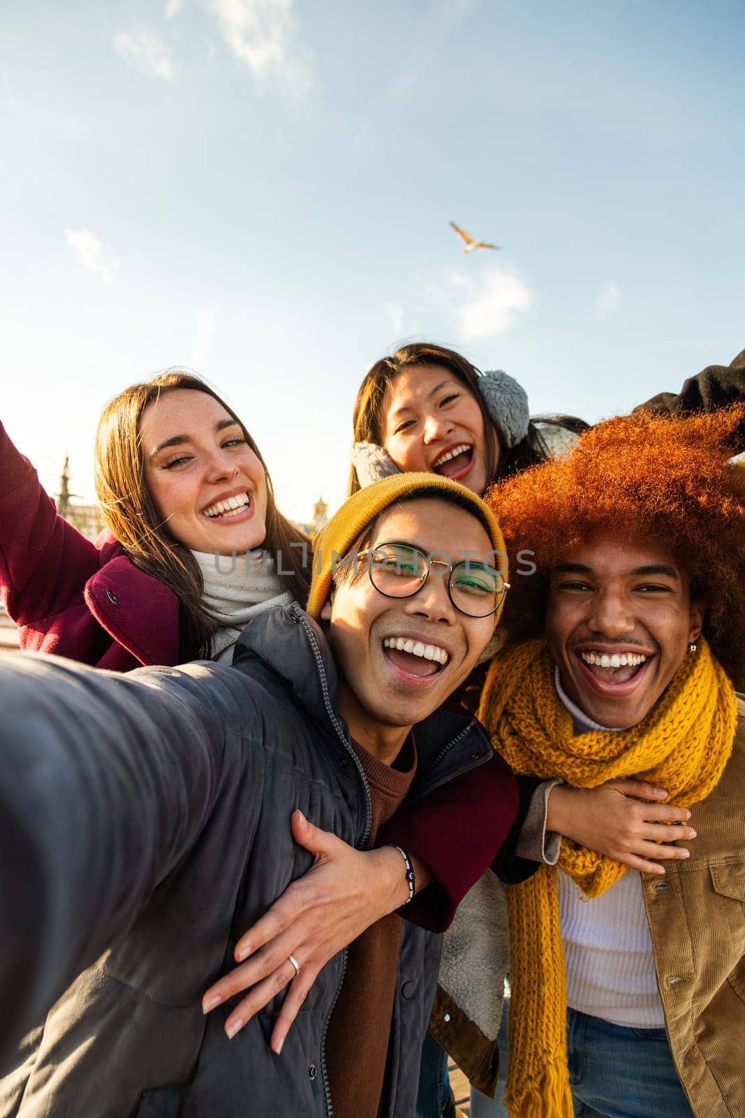 Selfie of multiracial happy friends enjoying winter day outdoors. Happy people looking at camera. Vertical. Copy space. by Hoverstock