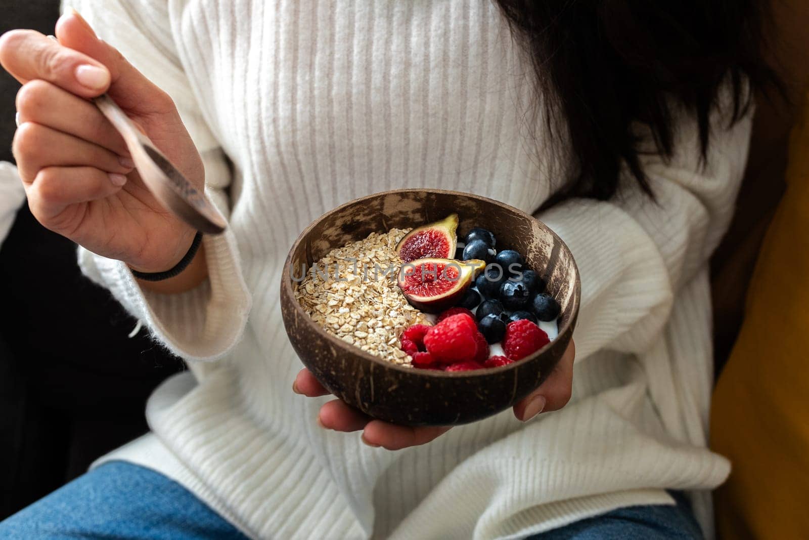 Close up of woman hand holding healthy breakfast smoothie bowl with granola oats, fresh berries and figs. Healthy lifestyle concept.