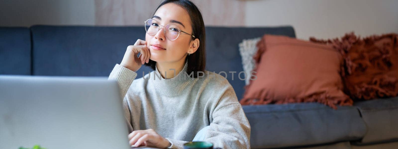 Self-employed young smiling woman, freelancer staying at home, working on remote from laptop, wearing glasses, sitting in living room by Benzoix