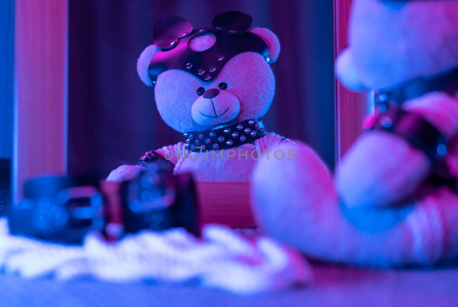 toy bear in leather harness and accessory for BDSM games on a dark background in neon light near the mirror by Rotozey