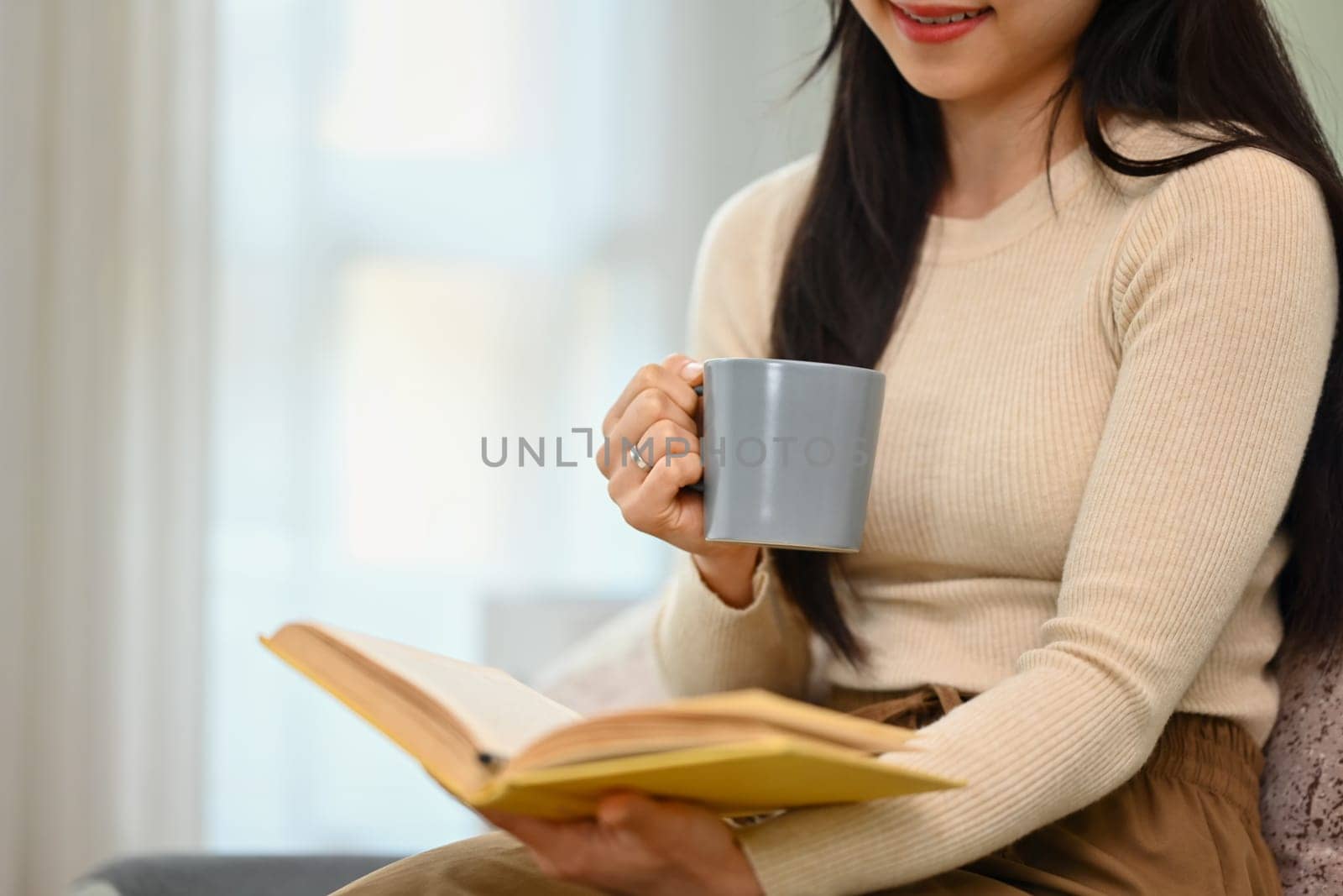 Carefree young woman drinking hot beverage in morning and reading book. People and lifestyle concept.