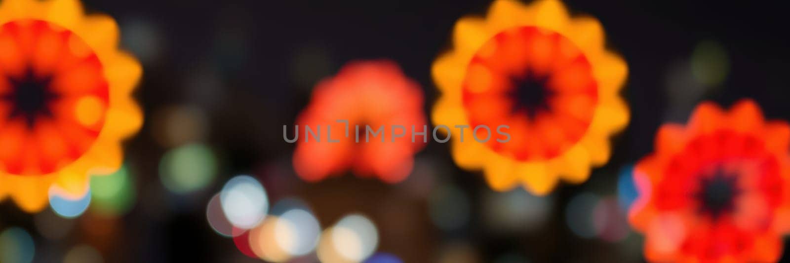 Brightly lit decorative lanterns in floral patterns create a lively atmosphere during a nighttime festival, surrounded by a dazzling city backdrop.