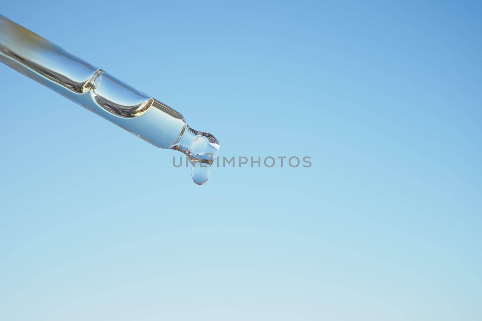 A single droplet gracefully hangs from a pipette set against a calm, serene blue backdrop