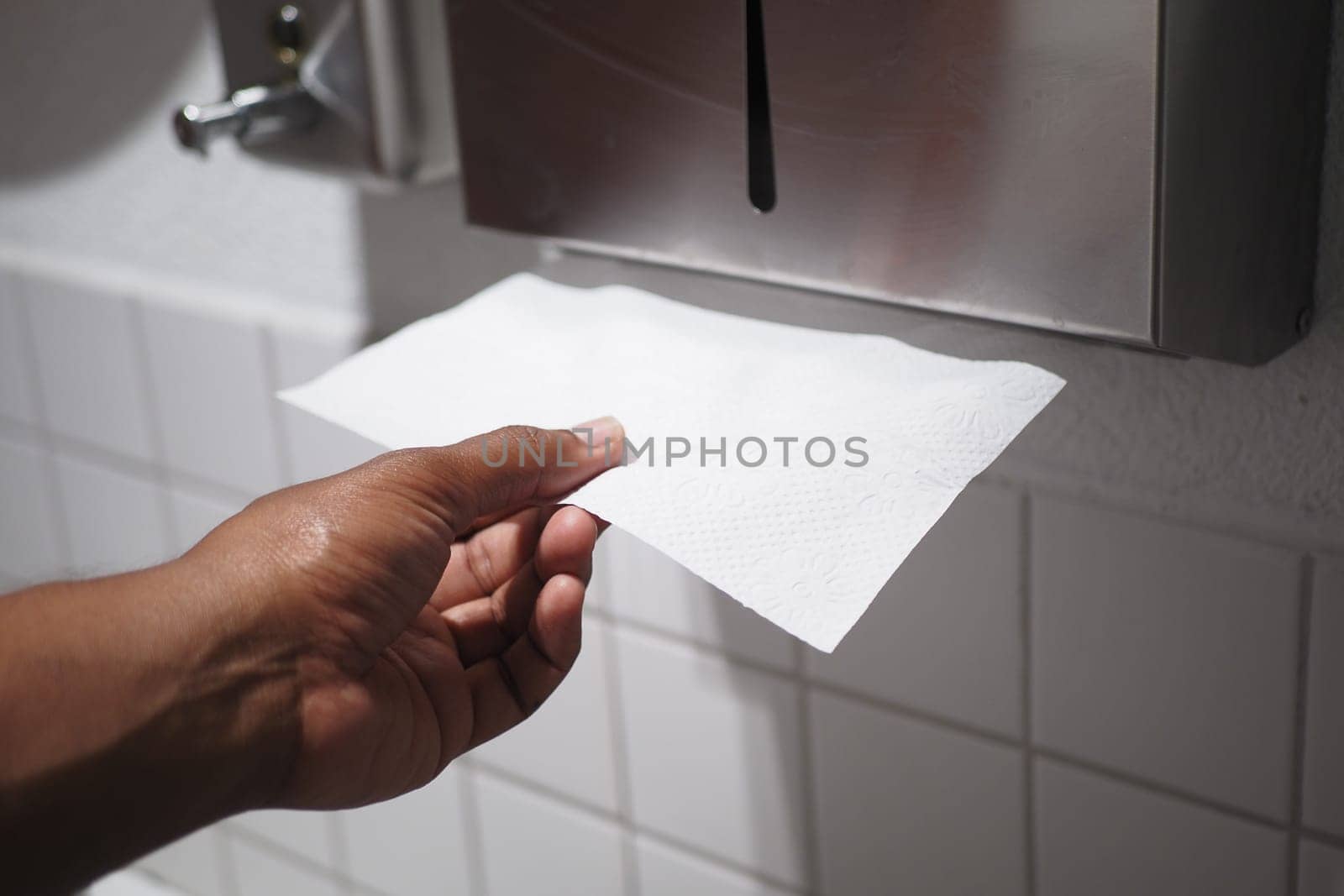 A hand reaches out and takes a paper towel from a tidy dispenser located in a clean restroom