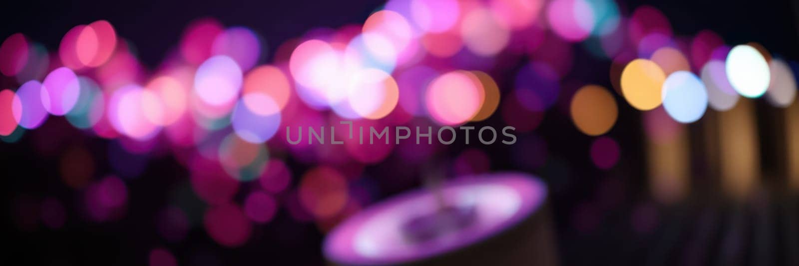 Colorful lights illuminate a festive evening gathering with people enjoying music, food, and camaraderie, creating an enchanting atmosphere filled with joy and excitement.