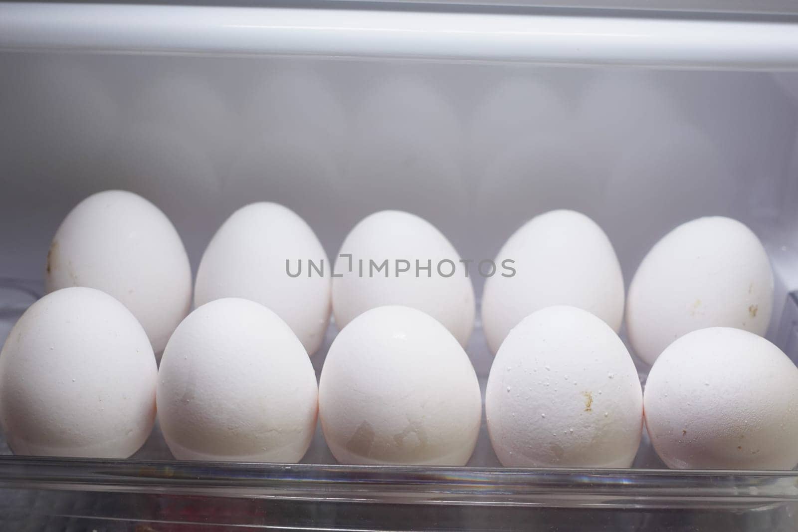 A total of ten fresh white eggs are meticulously stored in a clean refrigerator for safety