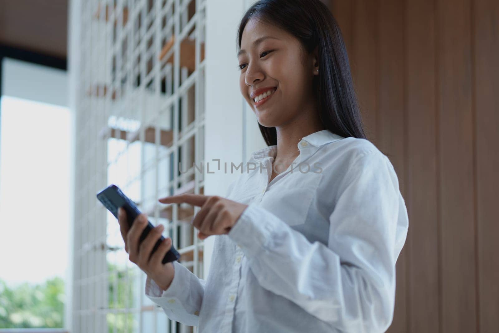 A young woman enjoys a moment of connection with her smartphone indoors, smiling as she interacts with technology and embraces modern lifestyle trends.