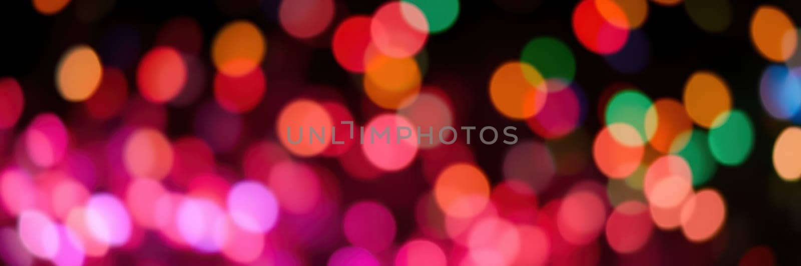 Radiant lights in various colors illuminate the night, contributing to a lively spirit during a local celebration. The vibrant hues create a magical background for festivities.
