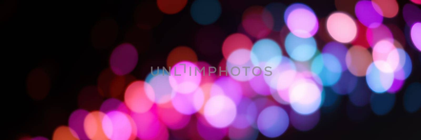 A collection of multicolored, blurred lights creates a festive ambiance in a bustling city during an evening event. The bright hues indicate a lively atmosphere.