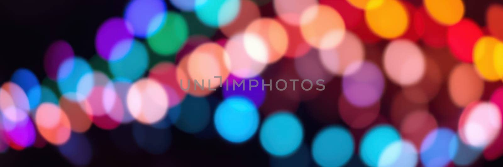 Bright, multicolored lights blur together, creating a lively atmosphere for a celebration in a city park during the evening. People gather to enjoy the festive ambience.