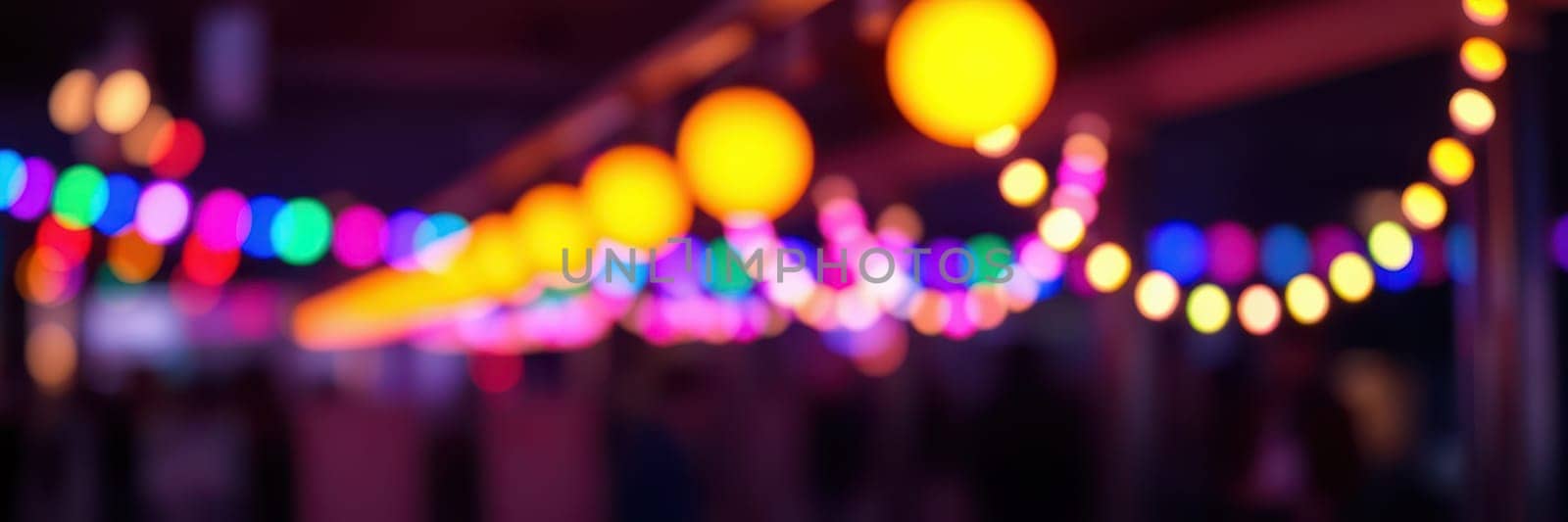 Festive string lights create a vibrant atmosphere at an outdoor event in the evening, illuminating the space with warm and colorful hues while people enjoy the celebration.