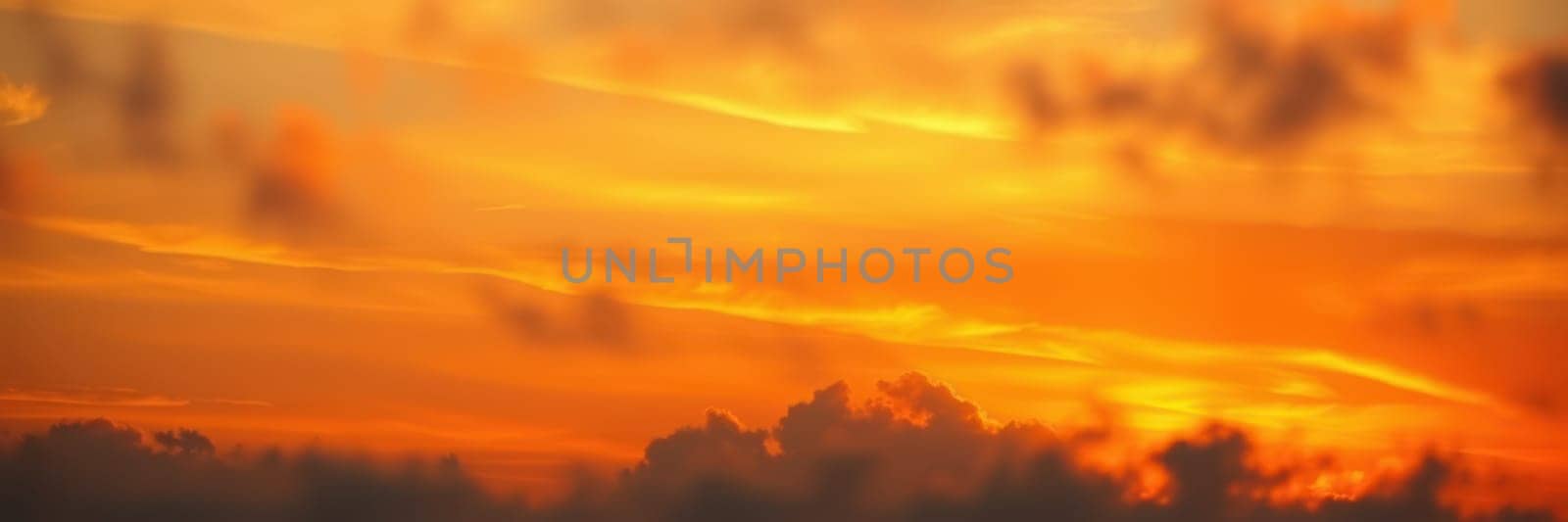 A stunning sunset spreads warm tones of orange and yellow across the sky, with clouds gently illuminated and silhouetted against the vibrant horizon during evening hours.