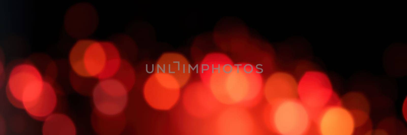 Warm red and orange lights twinkle softly in a blurred background, creating a cozy ambiance. The vibrant colors evoke feelings of joy during a nighttime celebration.