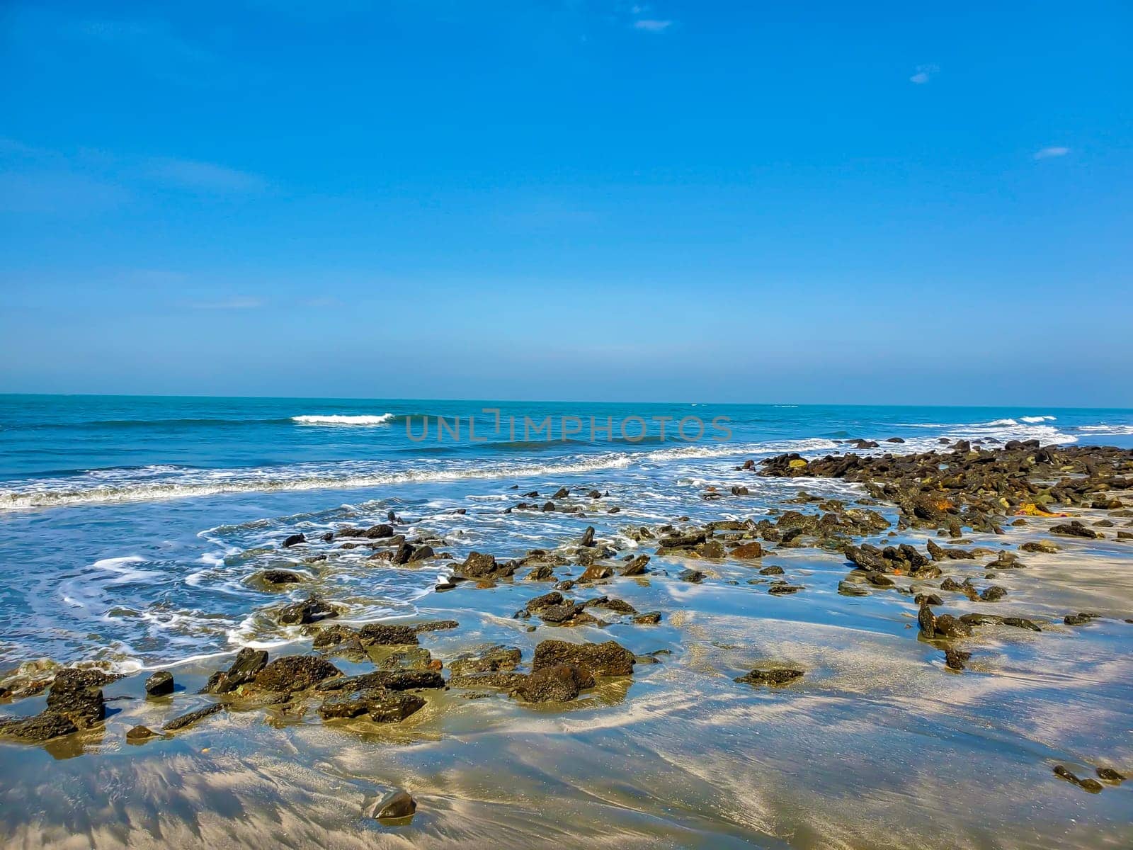 Rocky beach with waves washing around stones under a clear blue sky.
